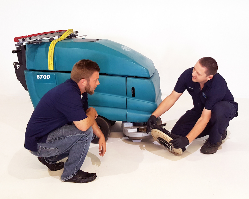 Floor cleaning tech showing person how to rotate a brush on Tenannt floor scrubber